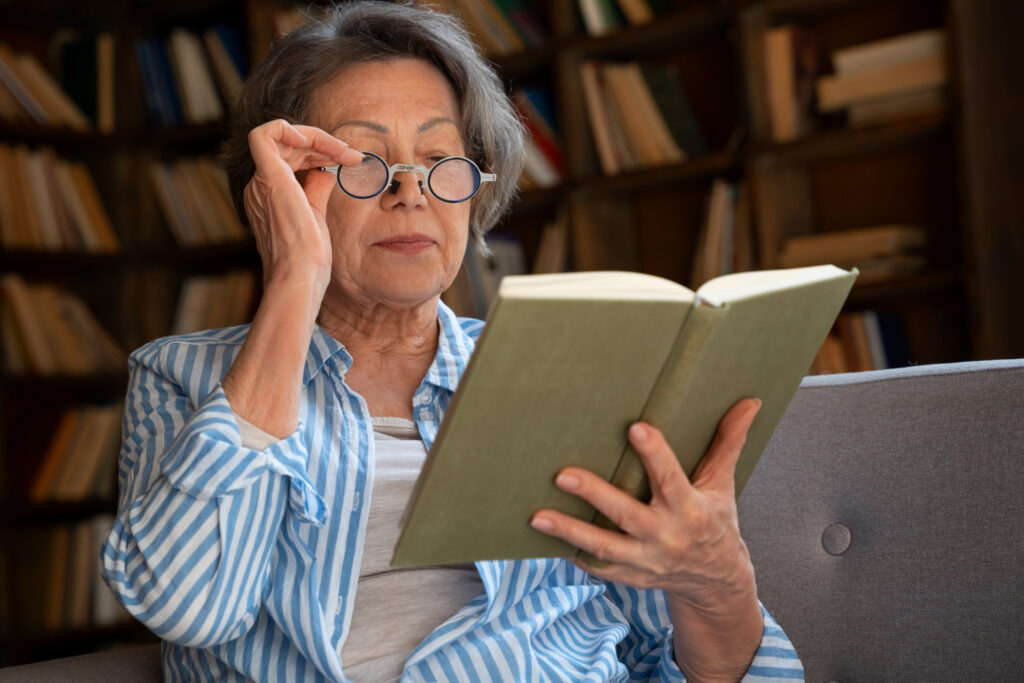 An elderly woman in a study, reading a book through her reading glasses
