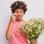 Woman feels unwell due to red eyes with kerchief suffers from seasonal allergy